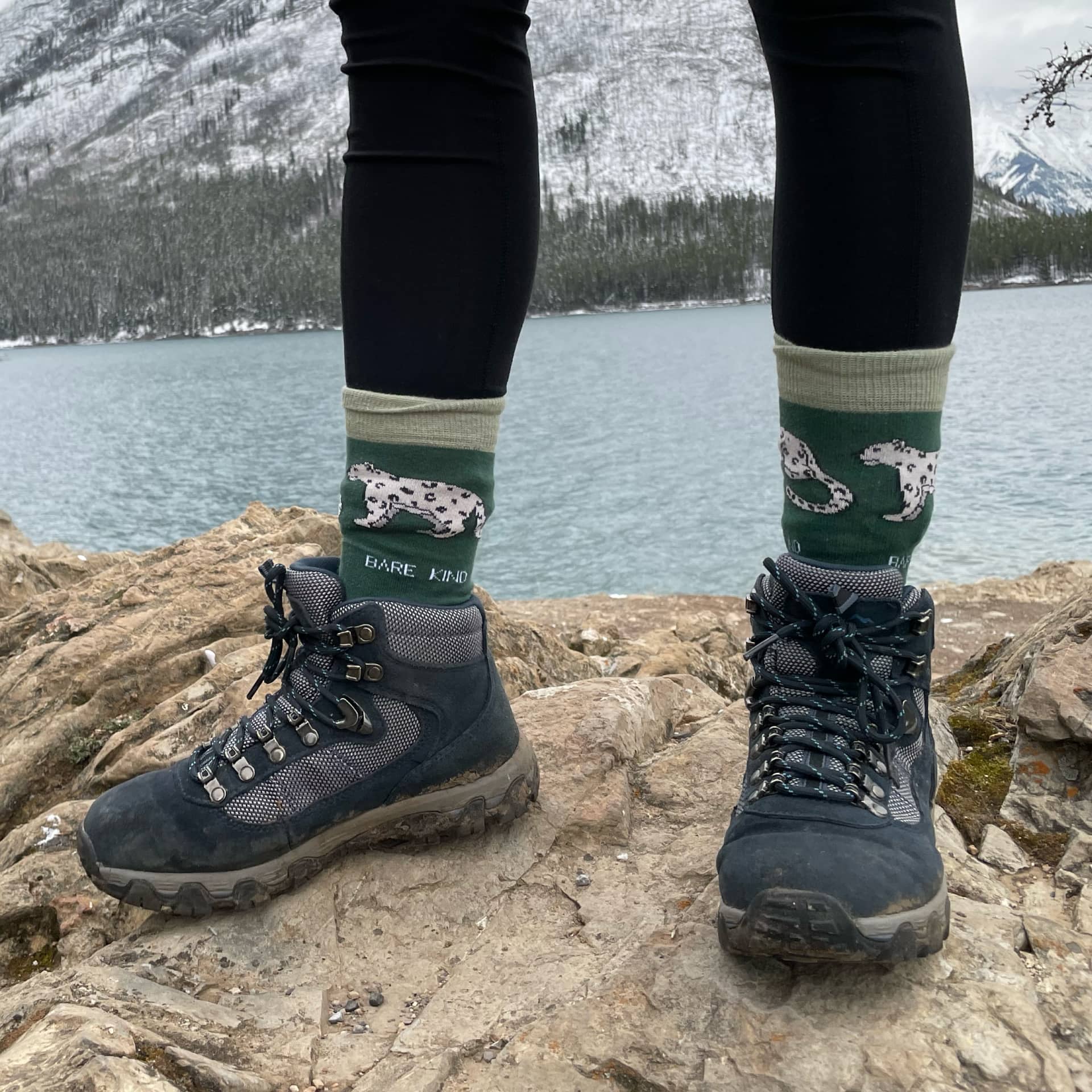 Person wearing hiking boots and socks with a mountain and lake background